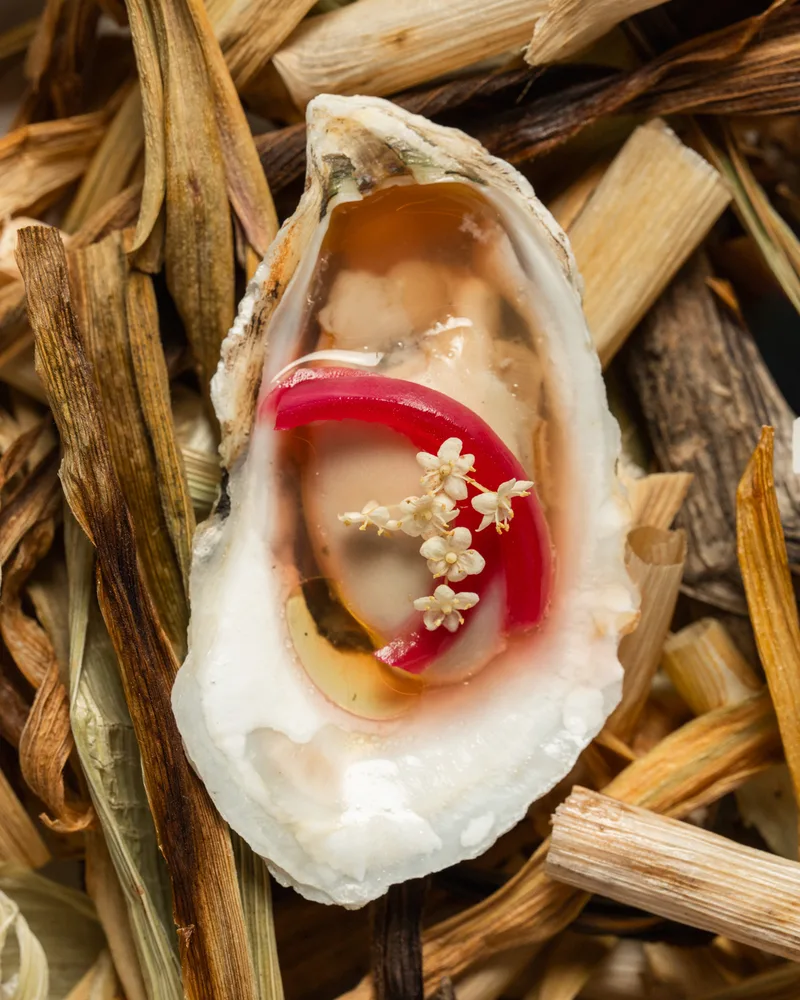 An oyster course dressed with pepper and blossoms, served on dried corn husks
